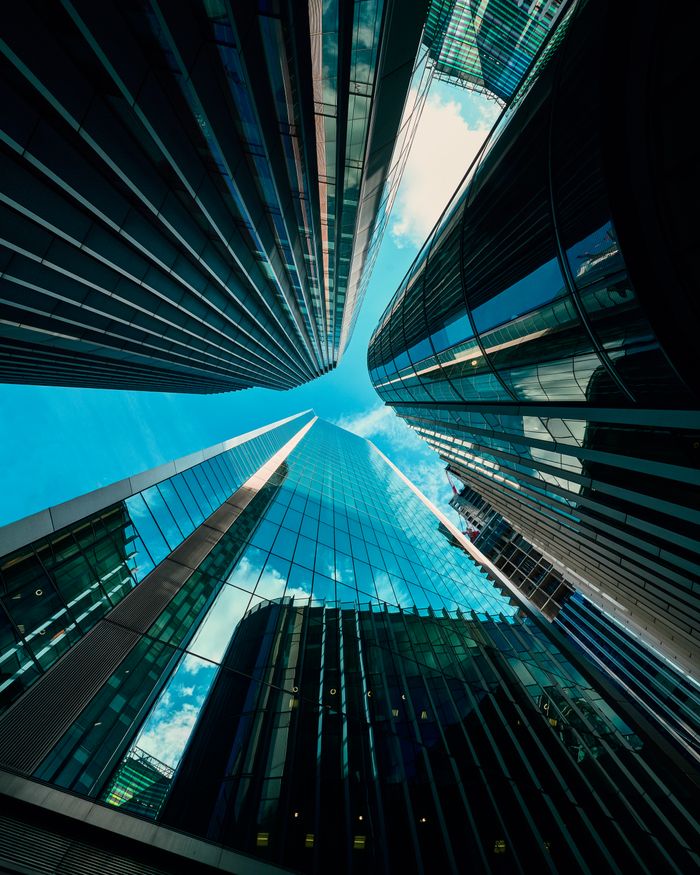 Low-angle view of modern skyscrapers reflecting the blue sky in a bustling urban area.